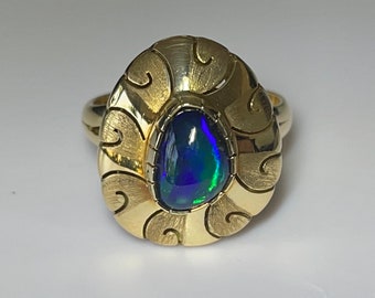May include: A gold ring with an intricate design featuring a blue and green opal gemstone.