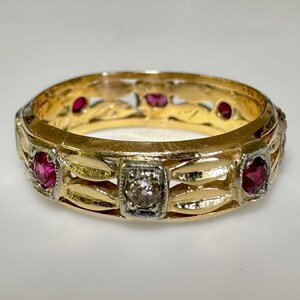 May include: A gold band ring with a delicate filigree design and five gemstones. The ring features four red rubies and one clear diamond.