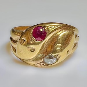 May include: A gold snake ring with a red ruby and a clear diamond. The ring is detailed with a textured snake design.