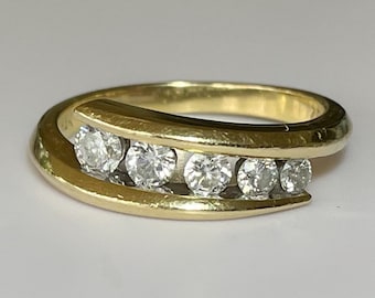Puede incluir: Un anillo de banda de oro con una fila de cinco diamantes redondos engastados en un diseño curvo.