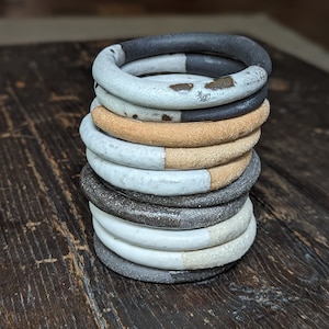 Peut inclure: Une pile d'anneaux en céramique dans différentes nuances de gris, blanc et beige. Les anneaux sont émaillés et ont une texture mouchetée.
