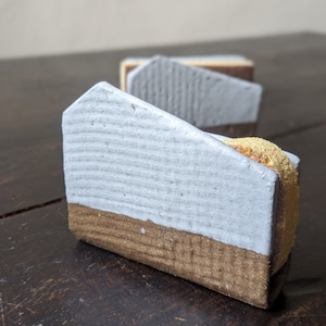 Peut inclure: Trois petits objets en céramique blanche en forme de maison avec une base en bois brun. Les maisons sont disposées en rangée sur une surface en bois brun foncé.