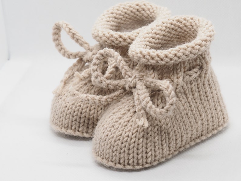 Pu&ograve; includere: Un paio di scarpine per neonati in maglia beige con un dettaglio a fiocco. Le scarpine sono realizzate in un filato morbido e caldo e hanno una vestibilit&agrave; comoda.