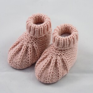 May include: A pair of pink knitted baby booties with a cable knit pattern.