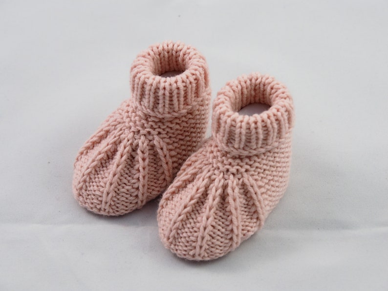 May include: A pair of pink knitted baby booties with a cable knit pattern.