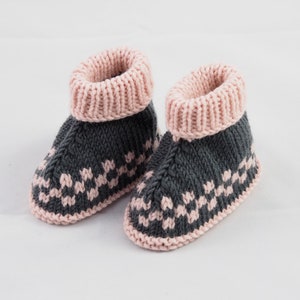 May include: A pair of knitted baby booties with a gray and pink color scheme. The booties have a pink cuff and a gray body with a pink geometric pattern.