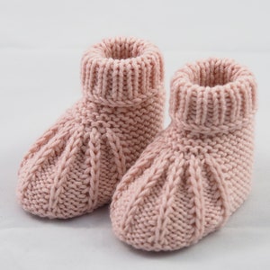 May include: A pair of pink knitted baby booties with a cable knit pattern.