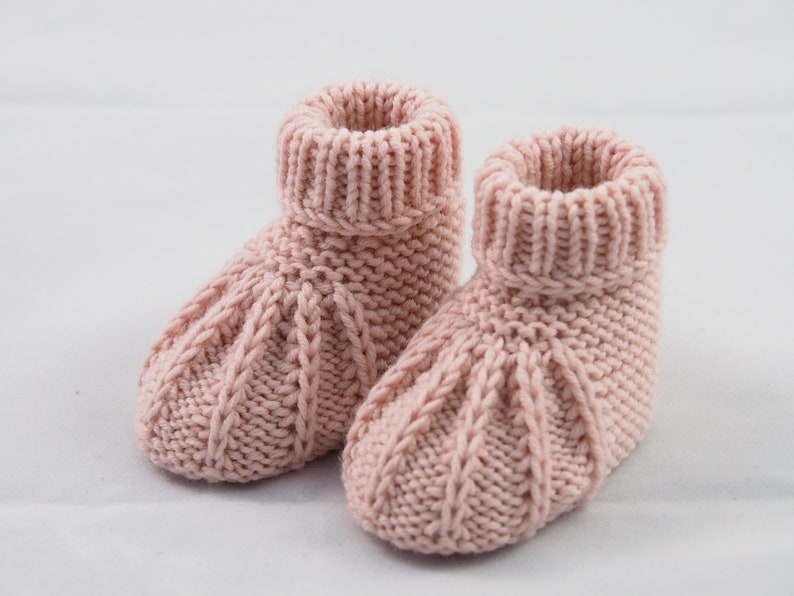 May include: A pair of pink knitted baby booties with a cable knit pattern.