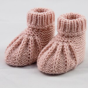 Ein Paar Babyschuhe vor weißem Hintergrund. Die Schühchen sind aus Wolle von Hand gestrickt. Sie wirken sehr stabil und warm. Am oberen Ende haben sie ein Rippenbündchen, das umgeschlagen wurde.