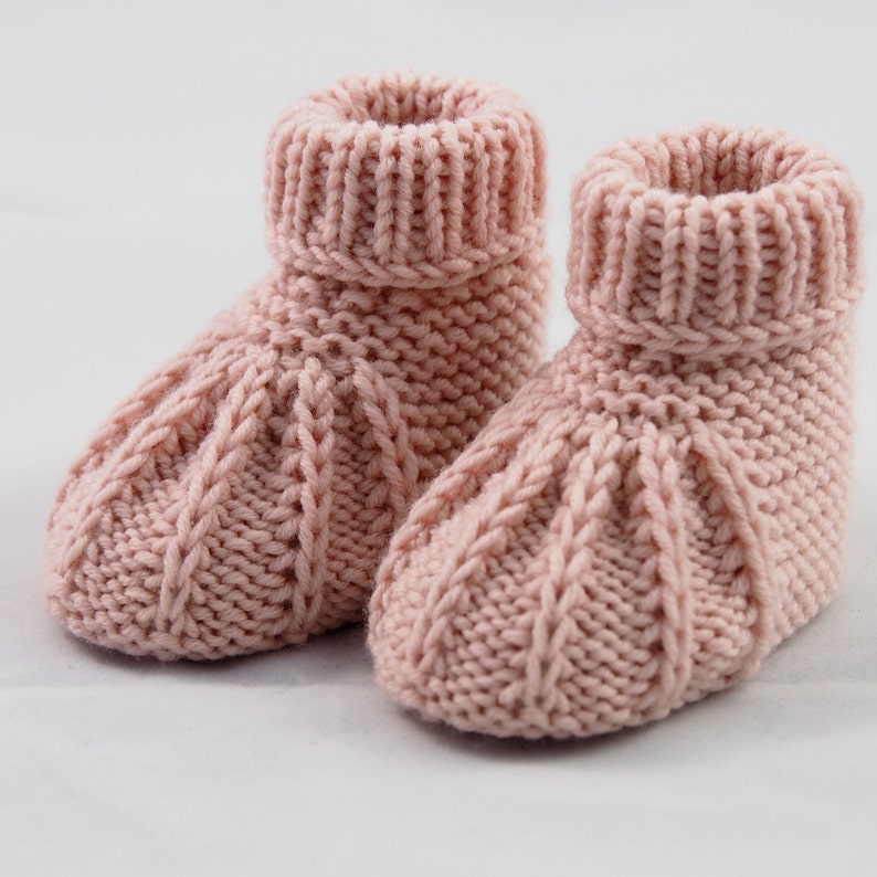 Ein Paar Babyschuhe vor weißem Hintergrund. Die Schühchen sind aus Wolle von Hand gestrickt. Sie wirken sehr stabil und warm. Am oberen Ende haben sie ein Rippenbündchen, das umgeschlagen wurde.