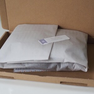 May include: A brown cardboard box with the lid open, revealing a white tissue paper package inside. The tissue paper is folded over and has a small white label with the text "Sweet Reads" on it.