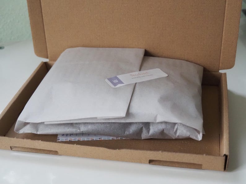 May include: A brown cardboard box with the lid open, revealing a white tissue paper package inside. The tissue paper is folded over and has a small white label with the text "Sweet Reads" on it.