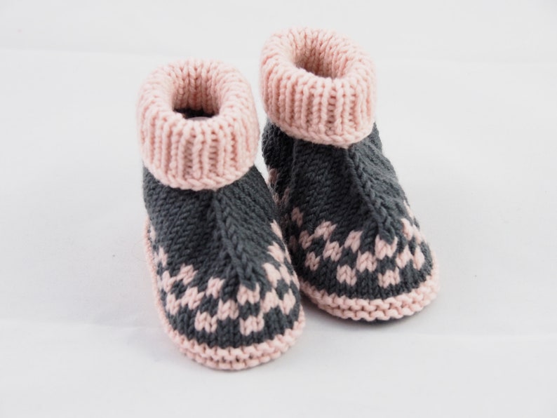 May include: A pair of knitted baby booties with a pink and gray color scheme. The booties have a pink cuff and a gray body with a pink pattern.
