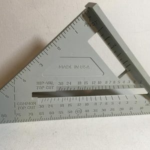 May include: A grey speed square with measurement markings and the text "MADE IN USA". The tool has a pivot and is designed for carpentry and construction. It features degree and centimetre measurements.