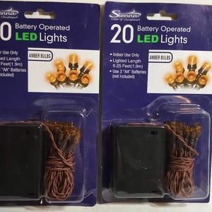May include: Two packages of Sienna Color of Christmas 20 battery operated LED lights with amber bulbs. Each package features a black battery pack, brown wire, and a lighted length of 6.25 feet. The packaging indicates indoor use only.