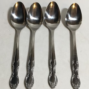 Può includere: Quattro cucchiai in acciaio inossidabile con superficie riflettente. Ogni cucchiaio ha un motivo floreale decorativo sul manico. I cucchiai sono disposti in fila, mostrando il loro design e la loro forma.