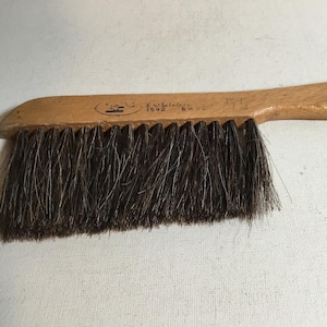 May include: A wooden hand brush featuring a long, light-colored wooden handle with a small hole at the end. The brush has dense, dark brown bristles attached to the underside. The handle displays faint stamped text including the number 1592.