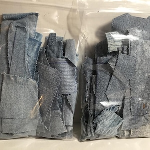 Puede incluir: Dos bolsas de plástico transparentes llenas de recortes de tela vaquera azul claro.