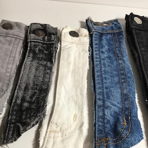 May include: Five different denim fabric strips in various shades of blue, gray, black, and white. The strips are frayed at the edges and have a raw, unfinished look.