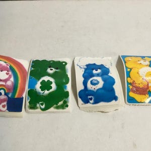 May include: Four Care Bear stickers featuring different Care Bears. The stickers are on a white background. The Care Bears are all smiling and have different colored fur. The Care Bears are all wearing different outfits. The stickers are all rectangular in shape.