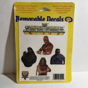 May include: A yellow card of removable decals featuring four WWF Superstars. The decals include images of wrestlers in action poses. The card also includes text that says "Removable Decals" and "Great For Bicycles, Locker Windows & Mirrors!!"