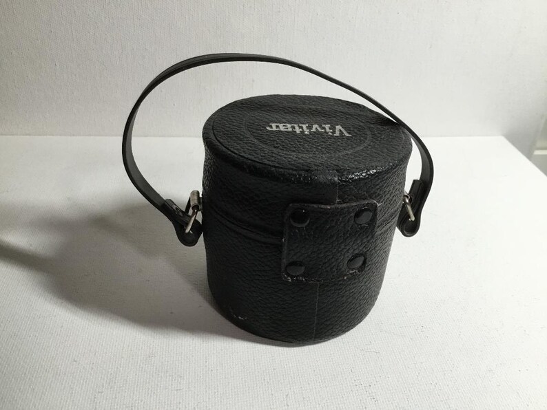 May include: A black leather camera case with a silver metal clasp and the word "Vivitar" embossed on the top.