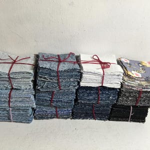 May include: Several stacks of fabric squares in different colours and patterns, including denim, white, and floral prints. Each stack is tied with red twine. The fabrics appear to be pre-cut for quilting or other craft projects.