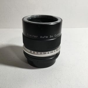 May include: A black Vivitar Auto 3x Custom lens with a silver aperture ring. The aperture ring has markings for f/22, f/16, f/11, f/8, f/5.6, f/4, f/2.8, and f/2.