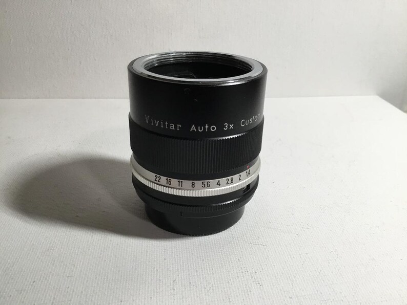 May include: A black Vivitar Auto 3x Custom lens with a silver aperture ring. The aperture ring has markings for f/22, f/16, f/11, f/8, f/5.6, f/4, f/2.8, and f/2.