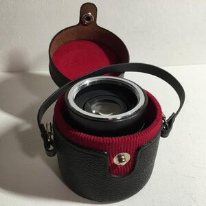 May include: A black leather case with a red interior holds a silver and black lens.