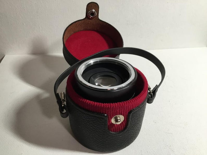 May include: A black leather case with a red interior holds a silver and black lens.