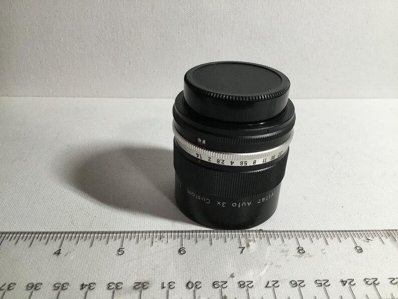 May include: A black camera lens with a silver ring and markings that read "Ultra Auto 3x Custom" and "17 8 55 4 28 2 14".