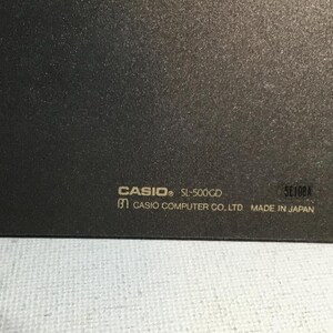 May include: Close-up of a dark gray electronic device with the brand name "CASIO" and model "SL-500CD" printed in white. The text "CASIO COMPUTER CO. LTD MADE IN JAPAN" is also visible.