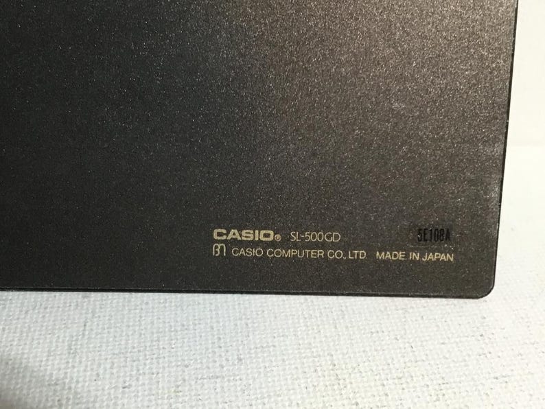May include: Close-up of a dark gray electronic device with the brand name "CASIO" and model "SL-500CD" printed in white. The text "CASIO COMPUTER CO. LTD MADE IN JAPAN" is also visible.