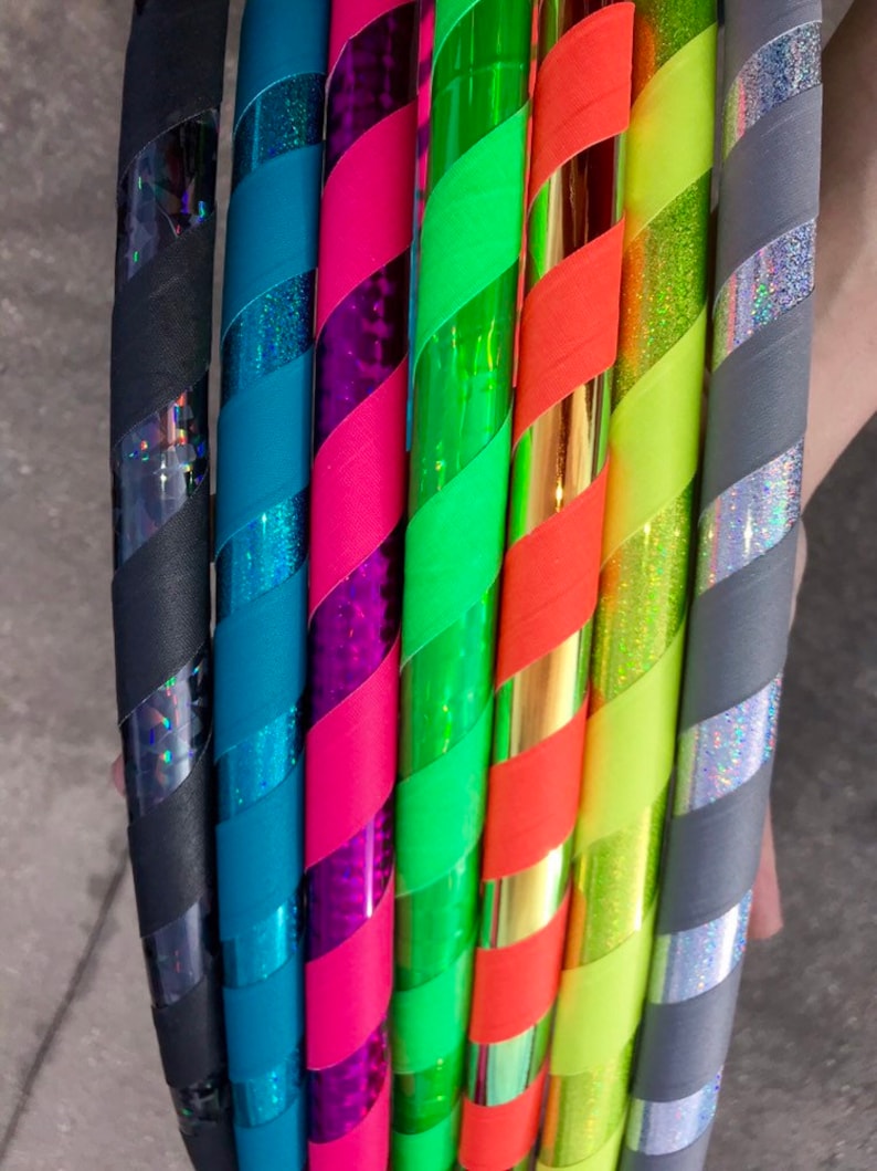 Op de afbeelding: Een set van acht kleurrijke hoelahoepringen met verschillende patronen en kleuren, waaronder zwart, teal, roze, groen, oranje, geel en grijs.