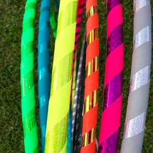 Op de afbeelding: Een verzameling kleurrijke, gestreepte hoepels met verschillende patronen en kleuren, waaronder groen, blauw, geel, oranje, roze en grijs.