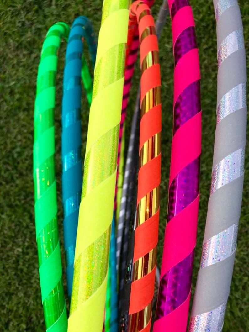 Op de afbeelding: Een verzameling kleurrijke, gestreepte hoepels met verschillende patronen en kleuren, waaronder groen, blauw, geel, oranje, roze en grijs.