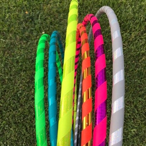 Op de afbeelding: Een groep kleurrijke hoelahoepringen met gestreepte patronen. De ringen zijn gemaakt van plastic en hebben een verscheidenheid aan kleuren, waaronder groen, blauw, geel, oranje, roze en grijs.