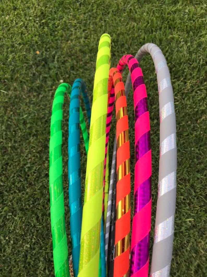Op de afbeelding: Een groep kleurrijke hoelahoepringen met gestreepte patronen. De ringen zijn gemaakt van plastic en hebben een verscheidenheid aan kleuren, waaronder groen, blauw, geel, oranje, roze en grijs.