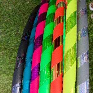 Op de afbeelding: Een set van zeven kleurrijke hoelahoepringen met verschillende patronen en kleuren, waaronder zwart, teal, roze, groen, oranje, geel en grijs.
