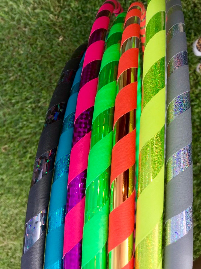 Op de afbeelding: Een set van zeven kleurrijke hoelahoepringen met verschillende patronen en kleuren, waaronder zwart, teal, roze, groen, oranje, geel en grijs.