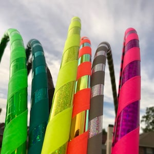 Op de afbeelding: Een set van zes kleurrijke hoelahoepringen met verschillende patronen en kleuren, waaronder groen, geel, oranje, grijs en roze. De ringen zijn gemaakt van plastic en hebben een glanzende afwerking.