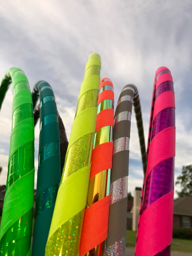 Op de afbeelding: Een set van zes kleurrijke hoelahoepringen met verschillende patronen en kleuren, waaronder groen, geel, oranje, grijs en roze. De ringen zijn gemaakt van plastic en hebben een glanzende afwerking.