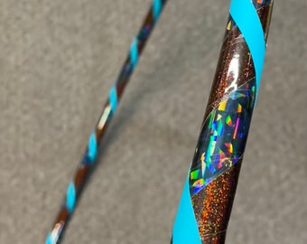 May include: A brown and iridescent hula hoop with a blue spiral design. The hoop is decorated with holographic glitter and blue tape, creating a visually appealing and dynamic look. This fitness accessory is designed for exercise and fun.