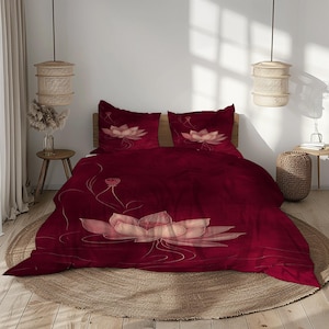 May include: A burgundy bedding set featuring a large lotus flower design. The set includes a duvet cover and two pillowcases, all with a floral print in shades of pink and cream. The bedding is displayed on a bed with a wooden headboard.