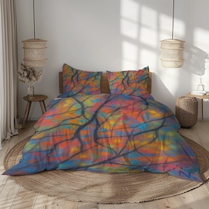 Op de afbeelding: Een kleurrijk beddengoed met een levendig abstract ontwerp. Het beddengoed omvat een dekbedovertrek en twee kussenslopen, met een patroon van boomtakken tegen een achtergrond van oranje, geel, blauw en rode tinten. De set wordt gepresenteerd op een bed met een houten hoofdbord.
