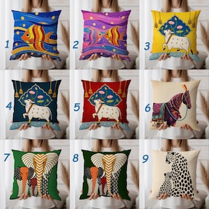 May include: Decorative throw pillows with various designs. Pillows feature colorful fish, a cow, an elephant, a horse, and a leopard. The pillows have a square shape and are held by a person.