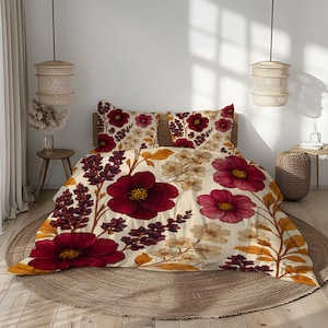 Pode incluir: Conjunto de roupa de cama floral com edredão e fronhas creme adornados com grandes flores bordô e rosa, acentuadas por folhagens amarelas e roxas. O design cria uma estética acolhedora e convidativa para o quarto.