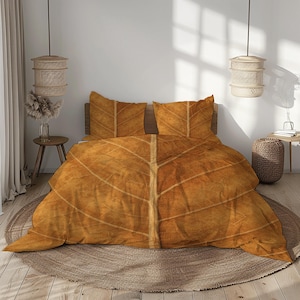 Può includere: Un letto con un copripiumino e due federe abbinate, con un motivo a foglia. La biancheria da letto è di un caldo colore marrone, con dettagli di venature, che ricordano una grande foglia. Il letto è posto su un tappeto rotondo intrecciato.
