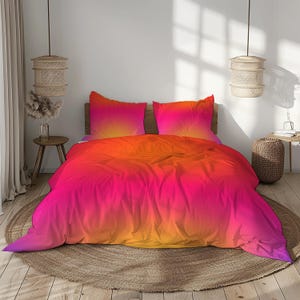 Könnte beinhalten: Ein Bettwäscheset bestehend aus einem Bettbezug und zwei passenden Kissenbezügen mit einem lebendigen Farbverlauf, der von tiefem Magenta und Pink an den Rändern zu einem leuchtenden Orange und Gelb in der Mitte übergeht.